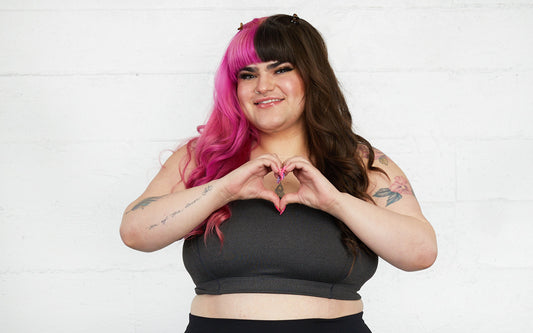 A cute model with pink and brown hair makes heart hands and smiles for a photo.