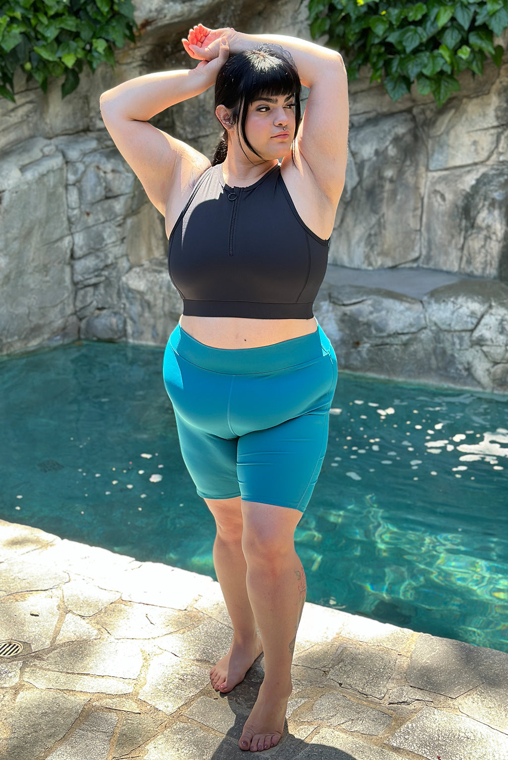 Full body of plus size model posing by pool wearing teal 9 inch swim shorts 