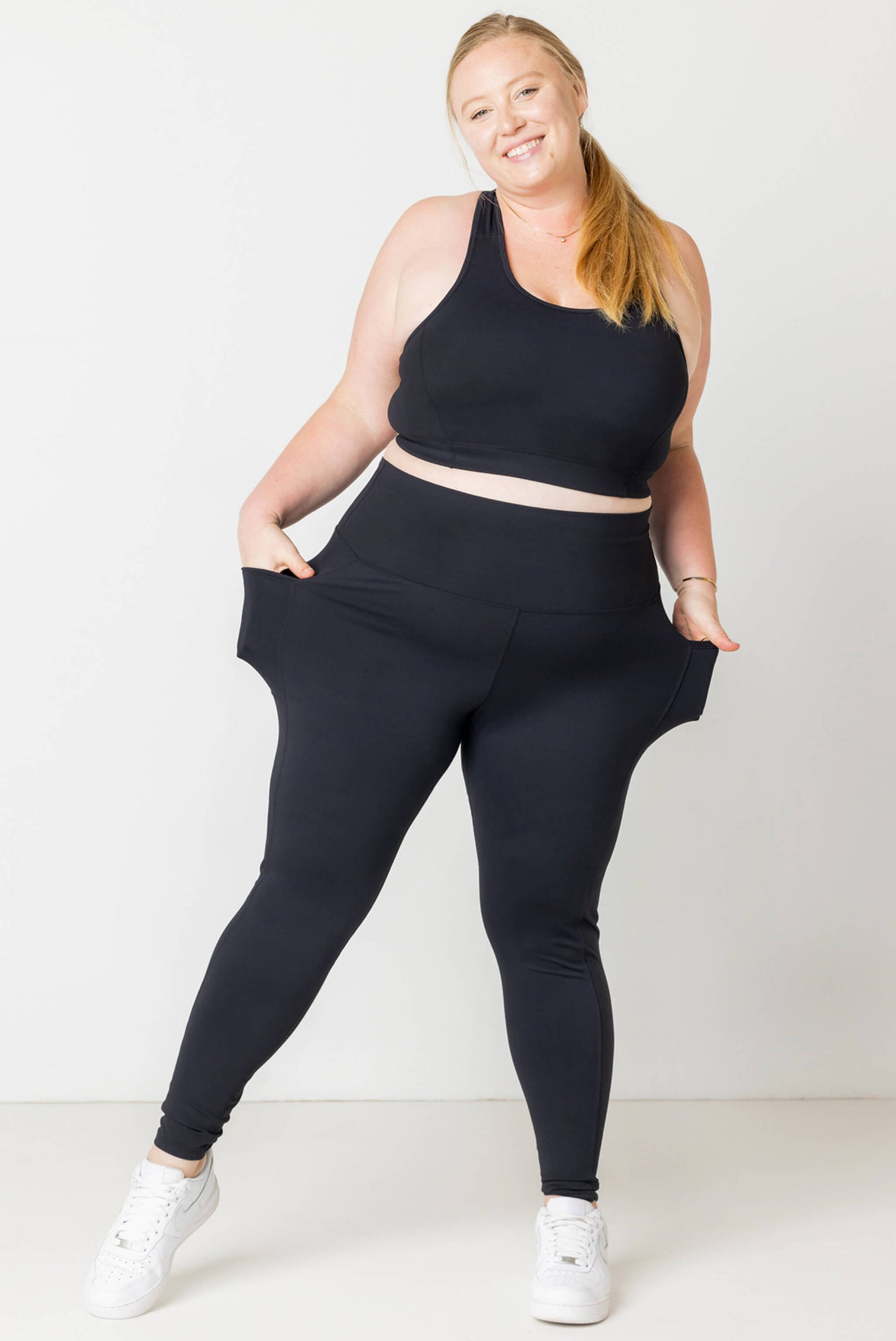 Smiling plus size model shows off the pockets on SuperHold ankle leggings in black.
