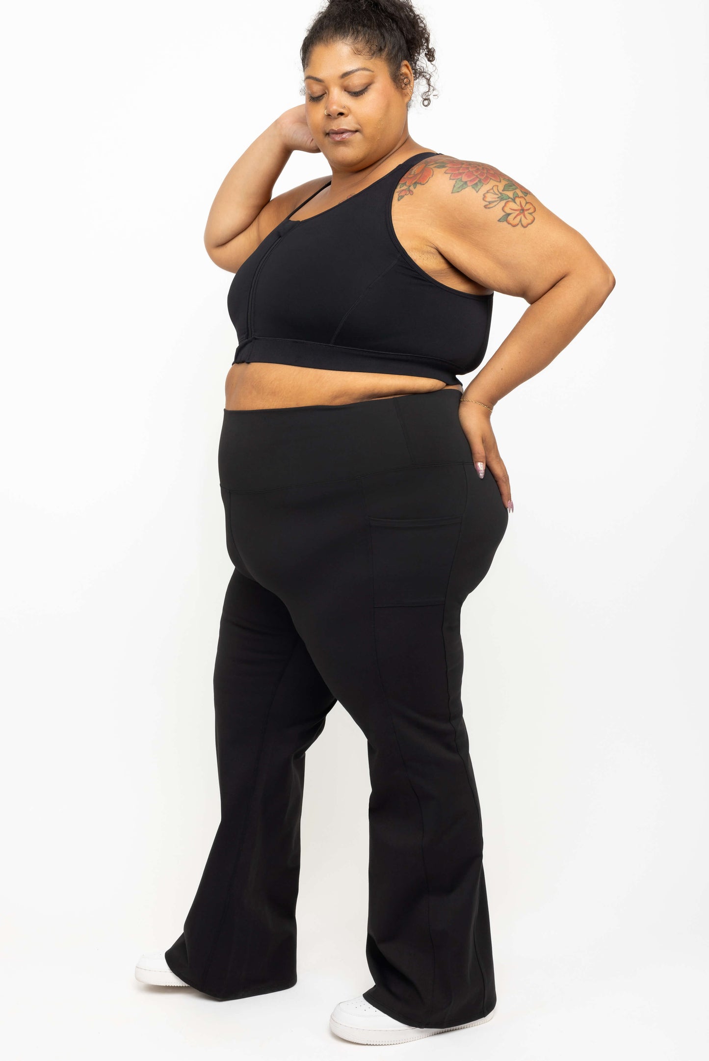 Profile view of model wearing Superfit Hero black plus size flare leggings with pockets size 3X