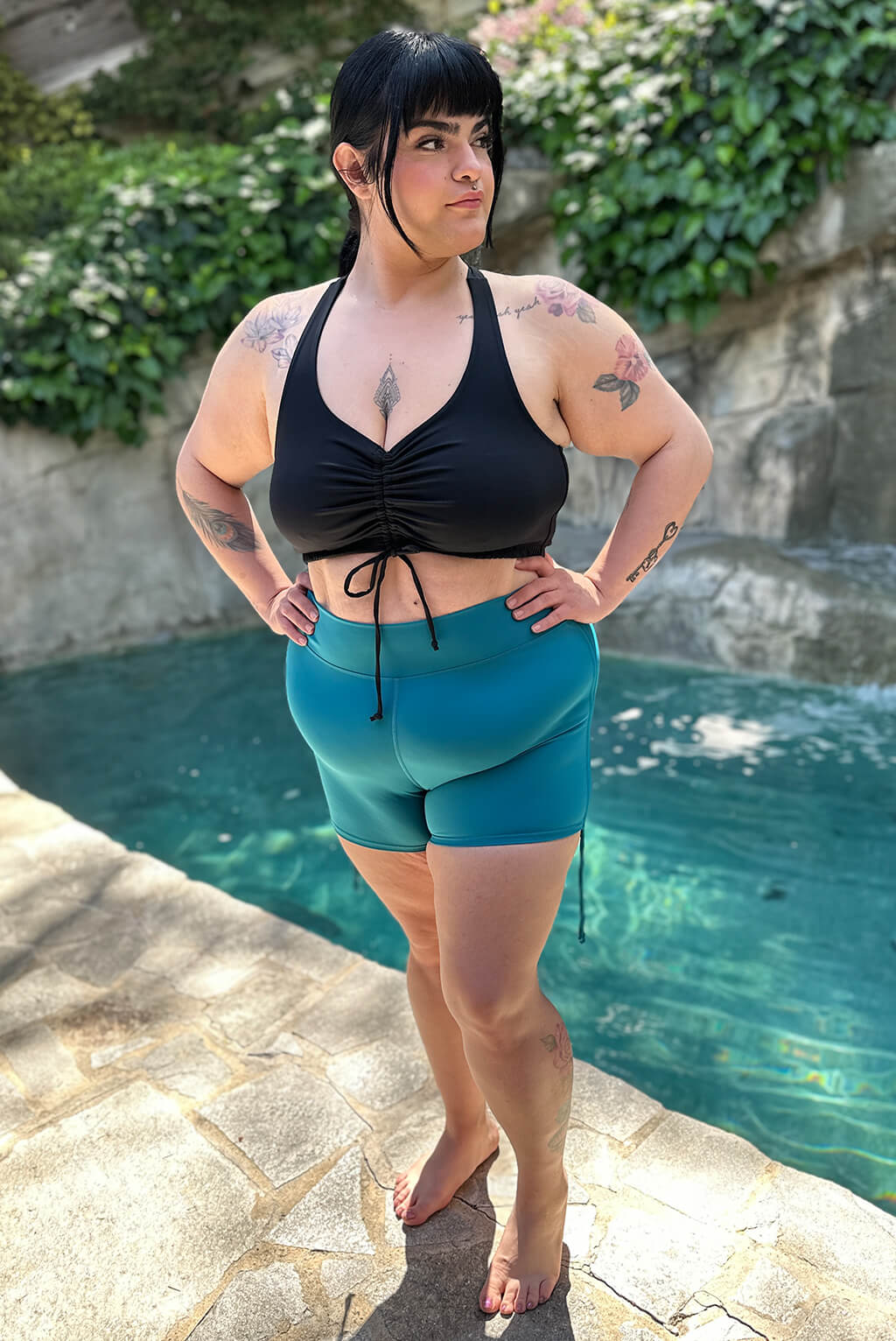 Front full body view of model wearing teal swim booty shorts with sides uncinched. 