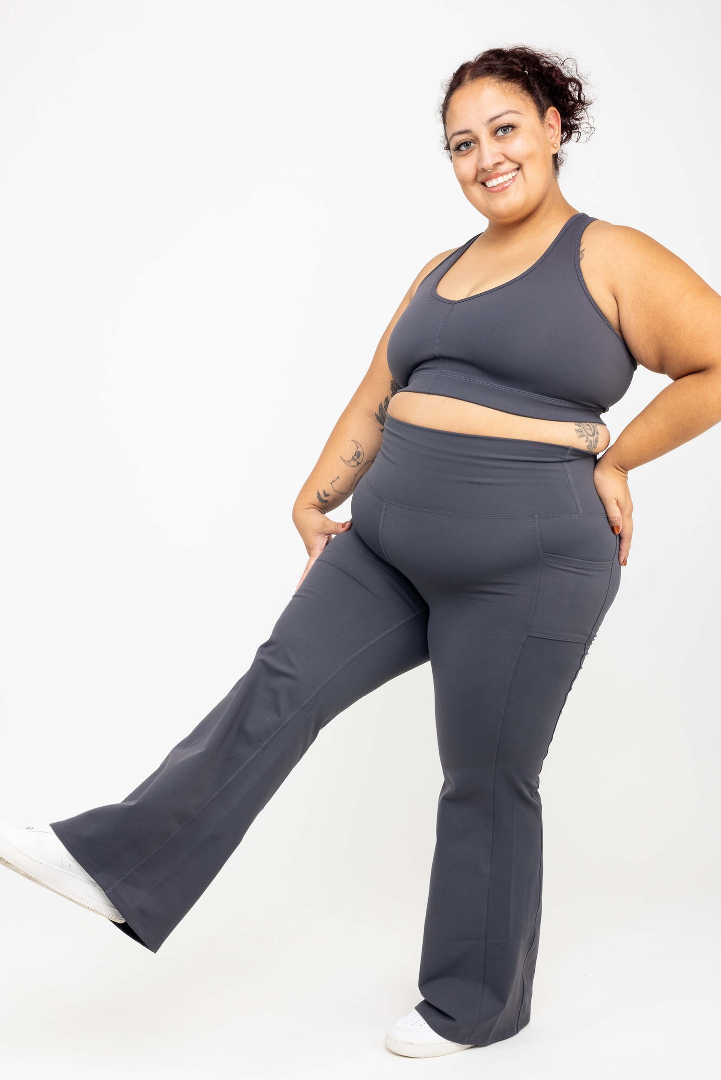 Model kicking her leg out wearing SuperHold™ Flare Pocket Leggings in Color Carbon, size 2X with matching V-neck Sports bra