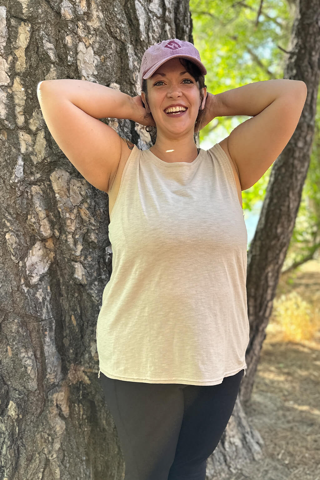 Model looks happy and puts her hands behind her head wearing textured muscle tank.