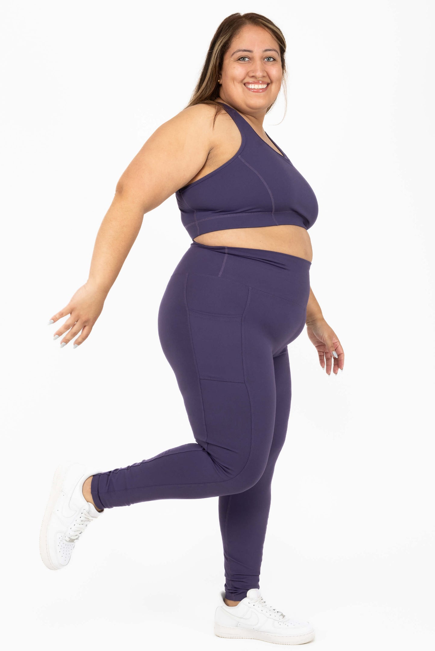 Side view of happy model kicking a leg up and wearing purple plus size leggings