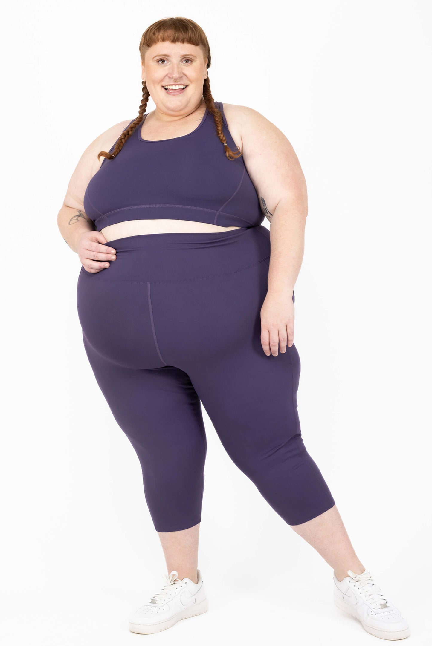 Plus size model posing in purple capris with pockets in purple compression fabric