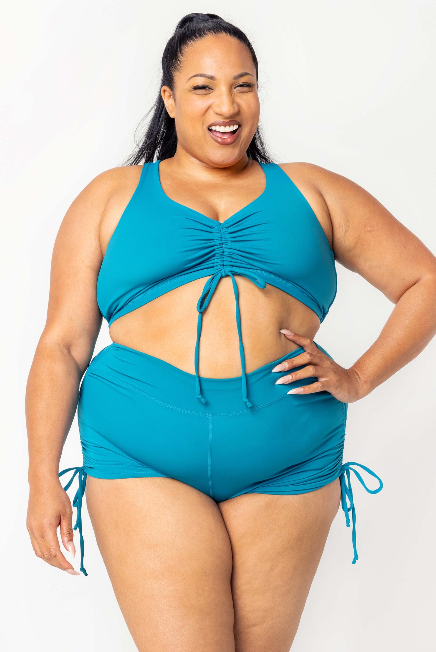 Front full body view of plus size model wearing cinched booty swim shorts and matching cinched bikini top in teal
