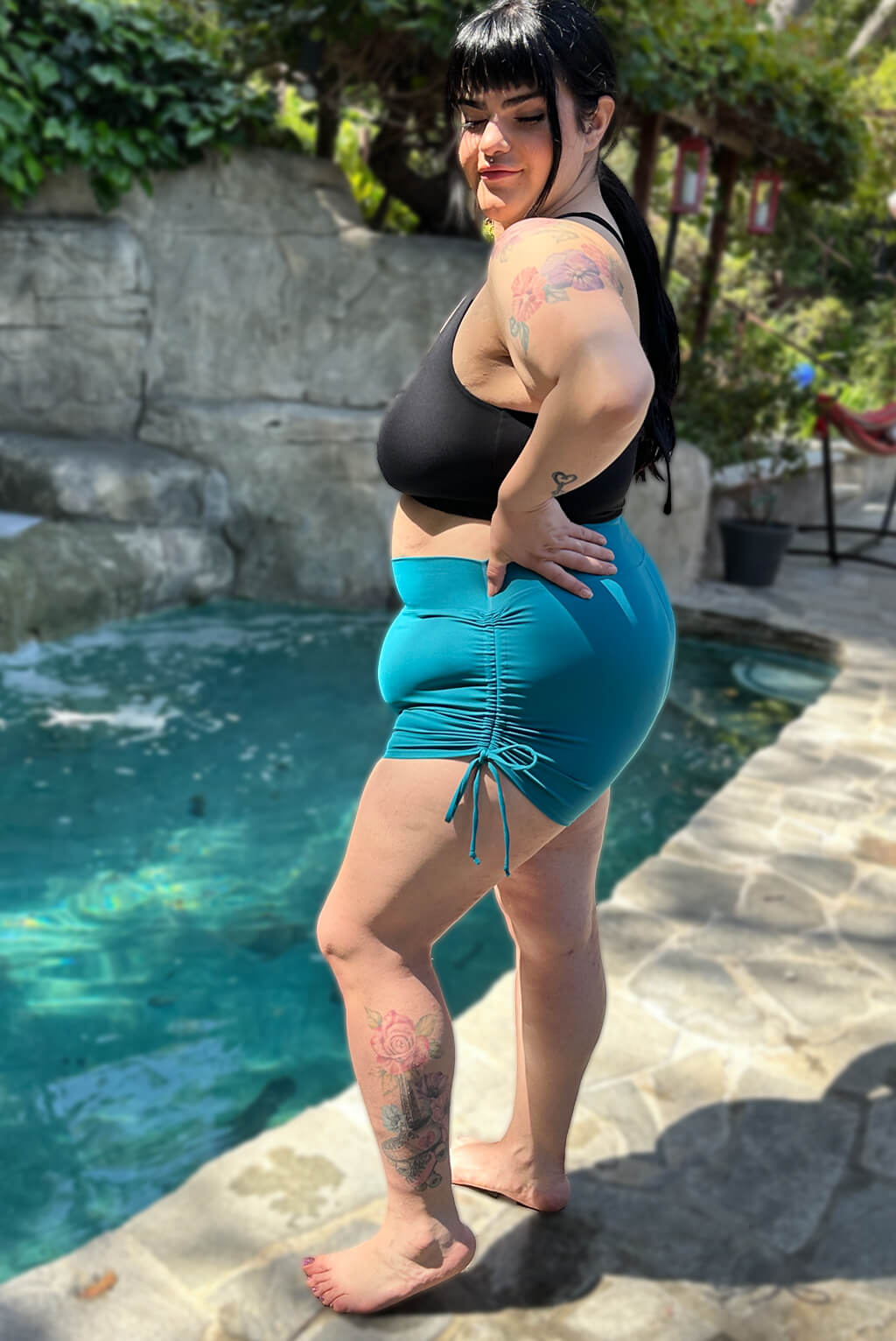 Profile view of model wearing teal swim booty shorts in size 2x.