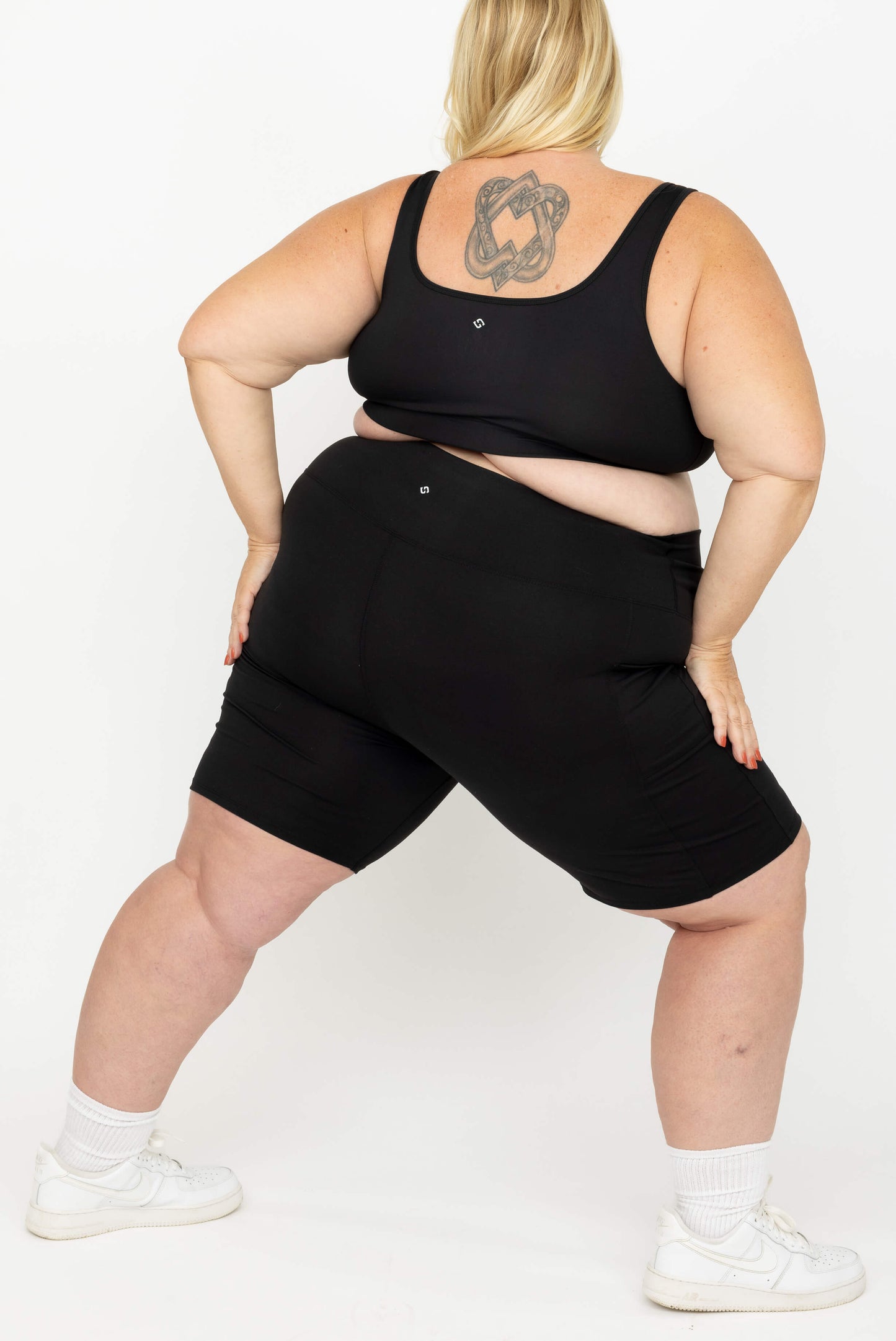 A plus-size model shown from the back wearing a Superfit Hero SuperHold Black Scoop Bra and matching shorts, against a plain white studio background.