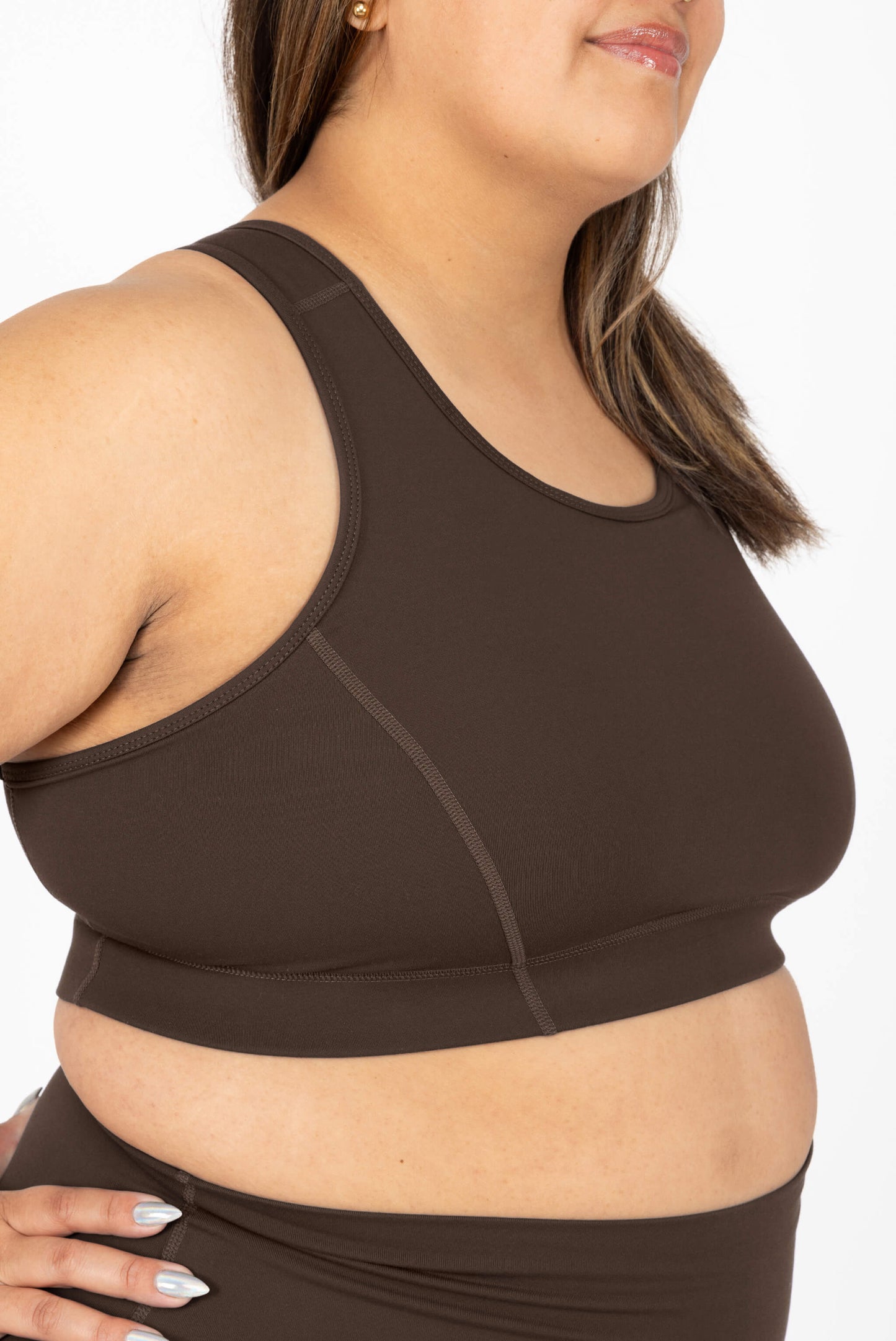 A close-up of a woman wearing SuperHold Racerback sports bra in Chocolate Brown and matching bottoms against a plain white background.
