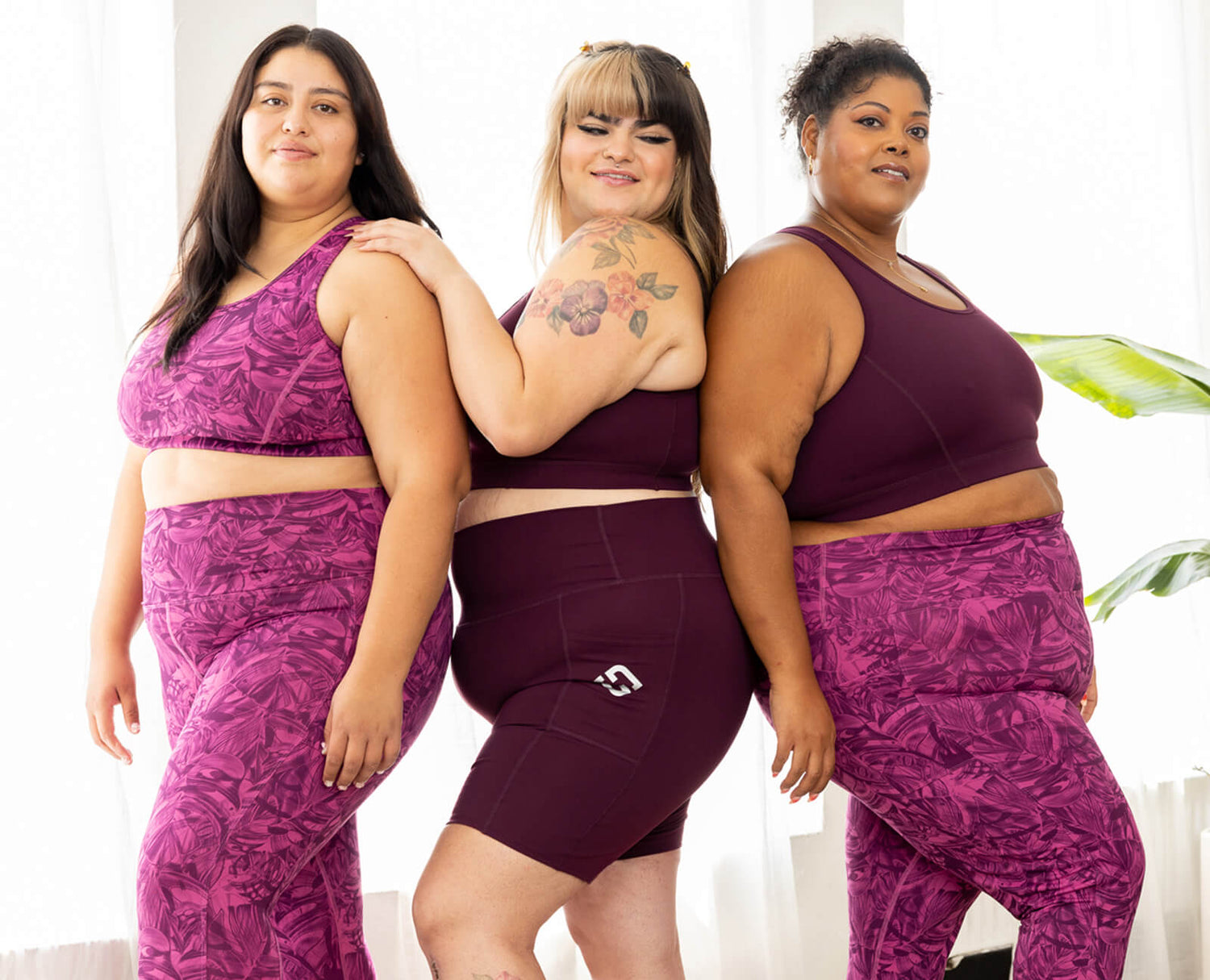 Three plus size models stand by each other in their plus size workout gear. Shelf tank tops and zip front compression sports bras.