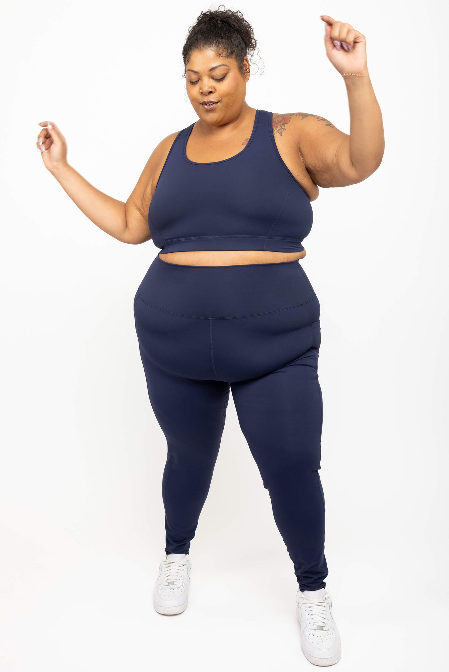 Model dancing while wearing Superfit Hero's high impact plus size racerback bra in size 3X, color navy