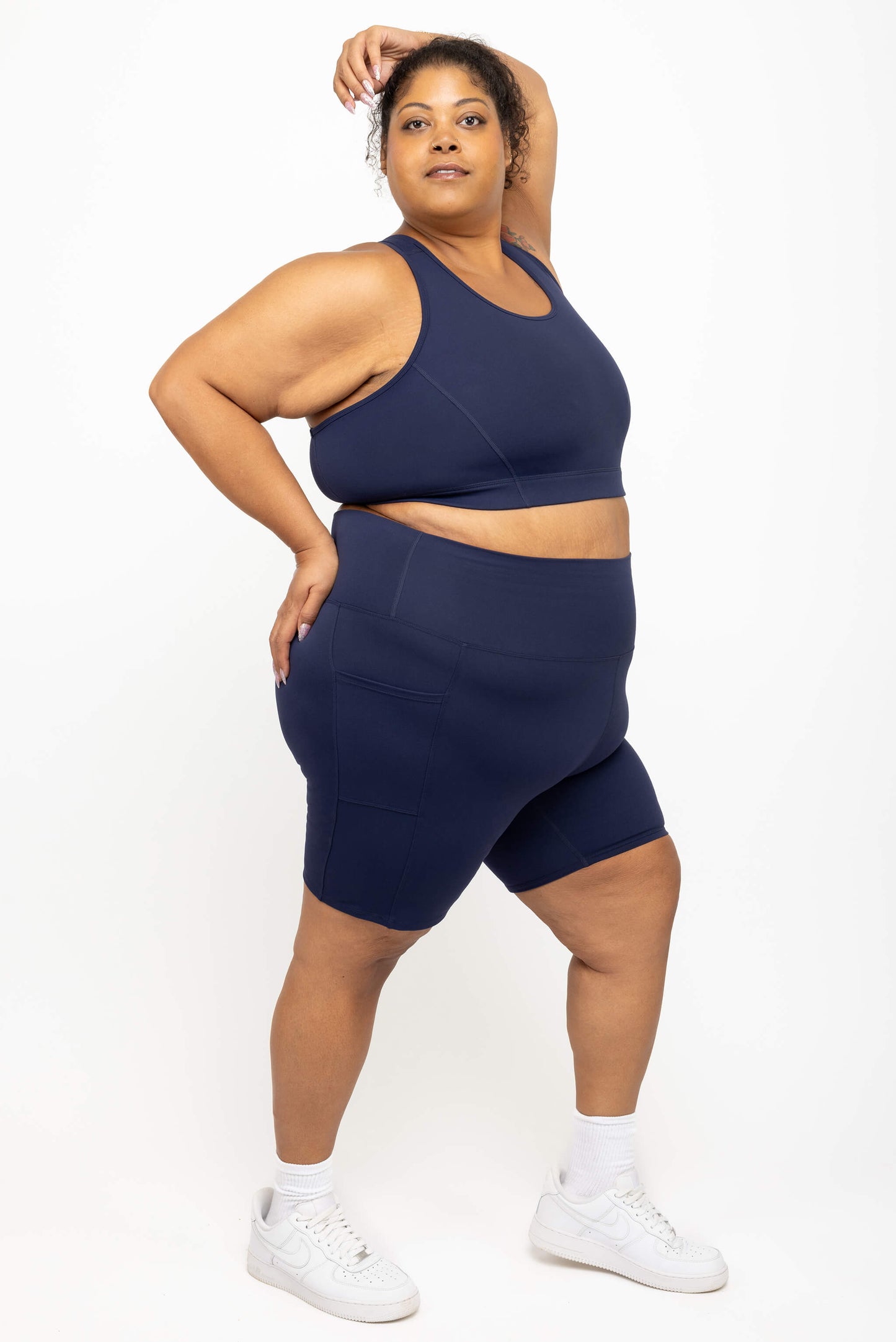 Model poses with arm over her head while wearing Superfit Hero's high impact plus size racerback bra in size 3X, color navy