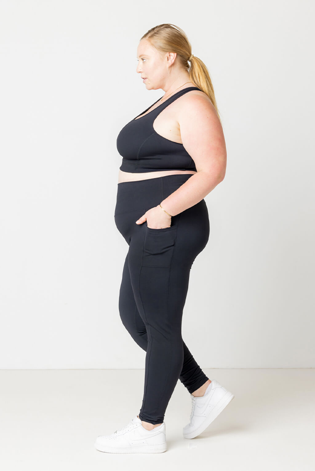 Profile shot of plus size model walking with her hand in the pocket of her Superfit Hero compression leggings.