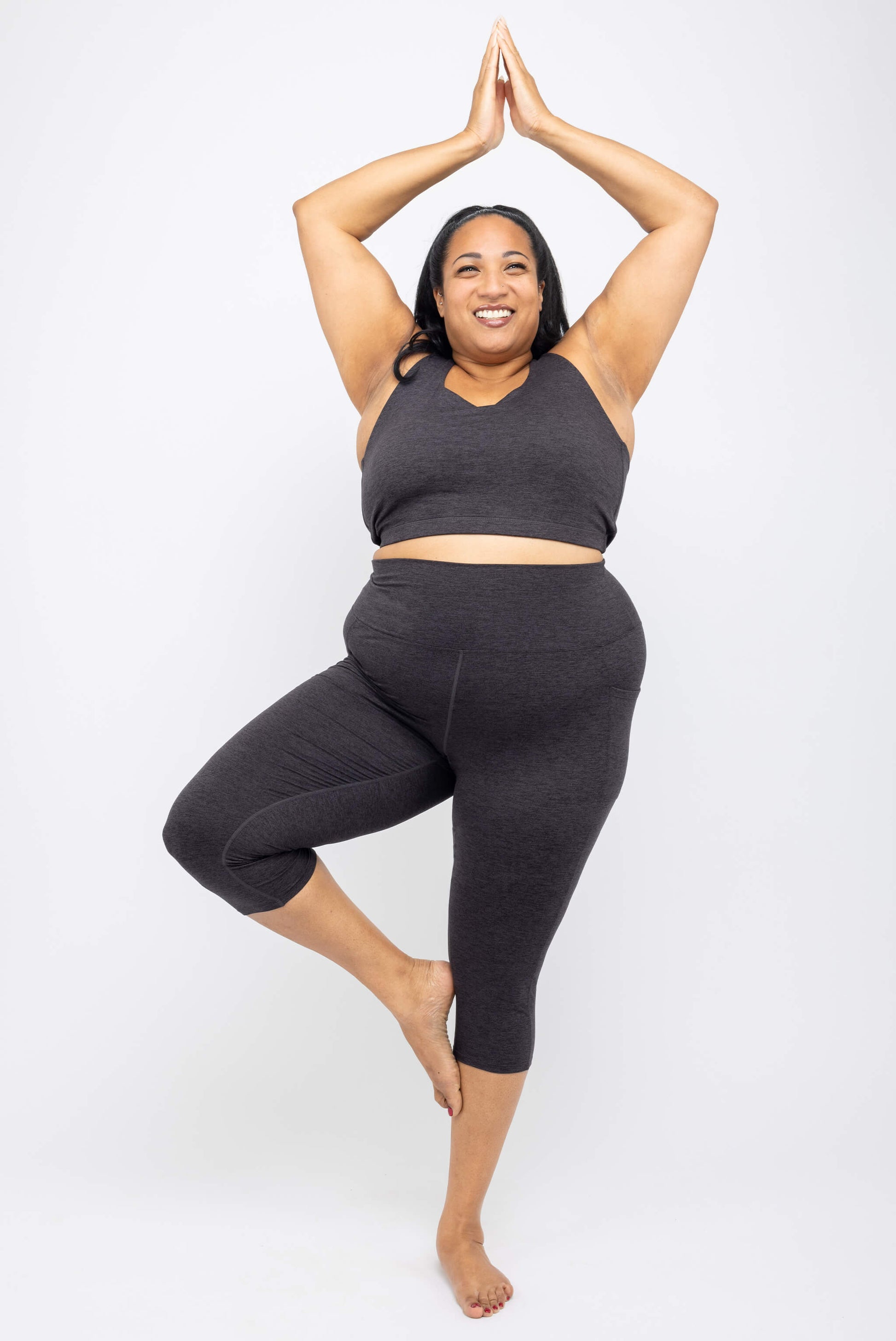 Model doing tree pose wearing Superfit Hero Plus Size SuperSoft Capri Leggings with Pockets