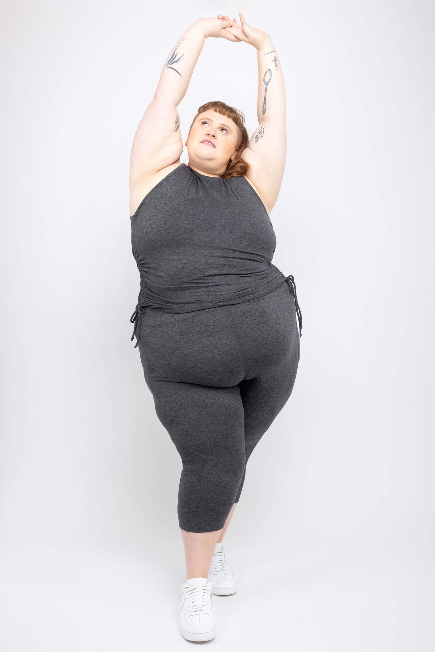 Plus size model poses with her arms up wearing size 5X SuperSoft Capri leggings and cinch tank