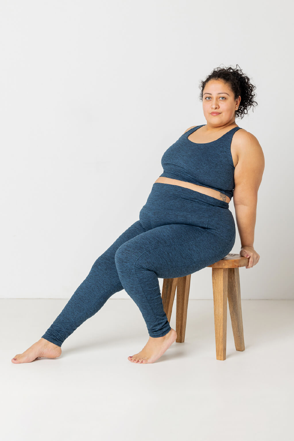 Plus size model sitting on wooden chair wearing Superfit Hero SuperSoft leggings in Heather Navy