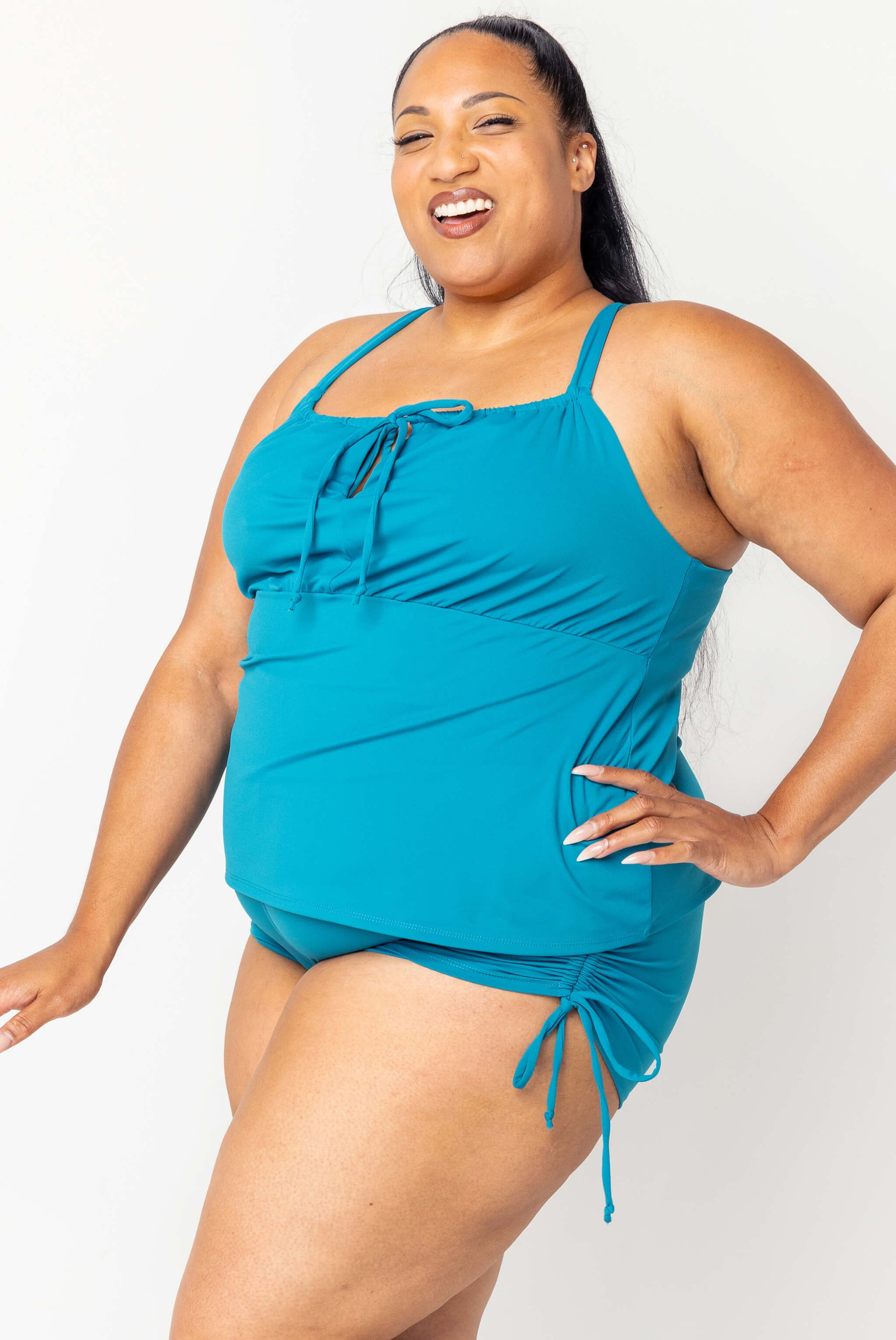 Profile view of Happy plus size model wearing teal swim tankini and matching booty shorts