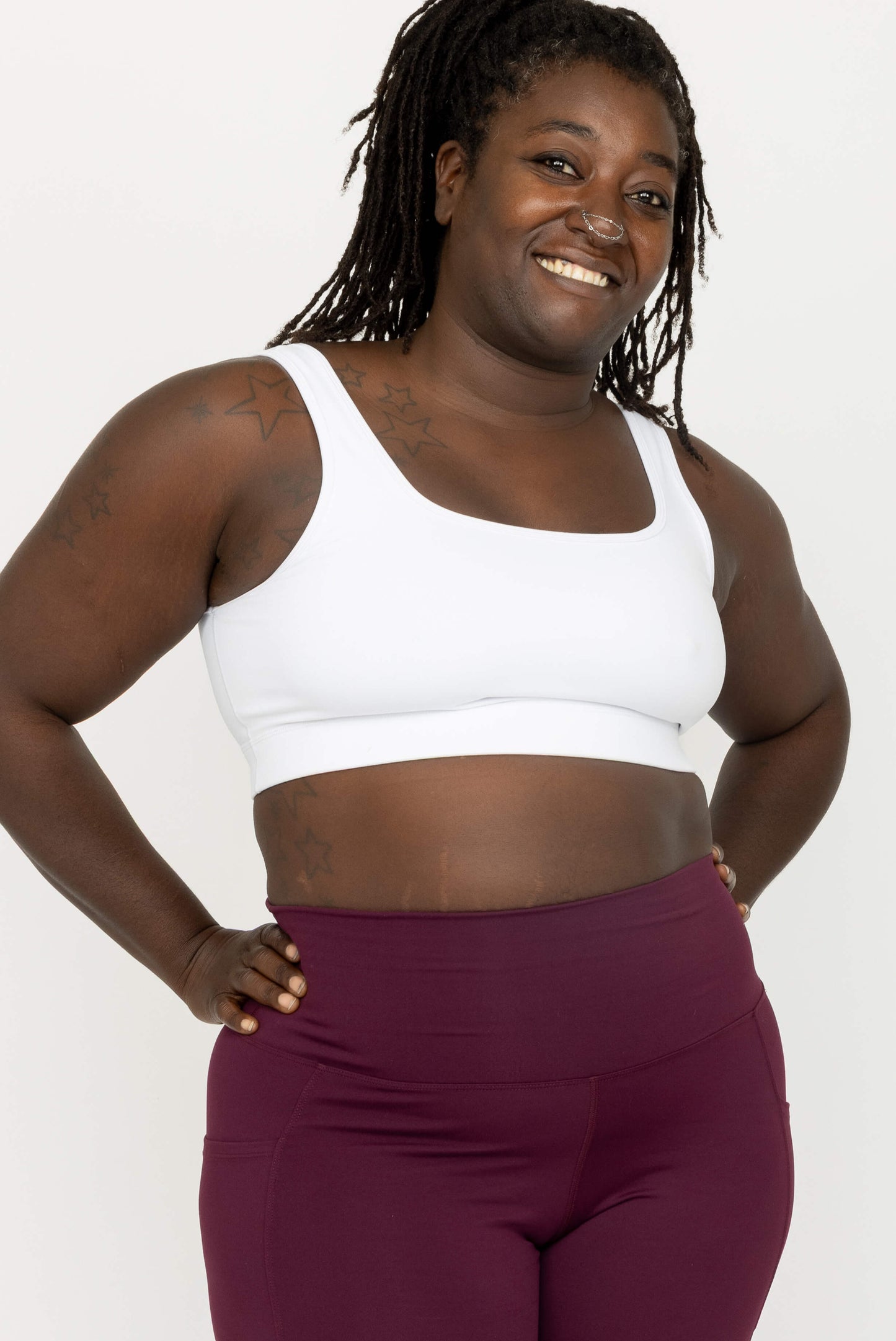 A woman modeling a white scoop-neck sports bra and high-waisted burgundy leggings against a plain white studio background.