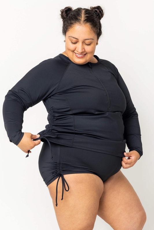 Size 2X model wearing plus size swim rash guard in black with the adjustable sides cinched up