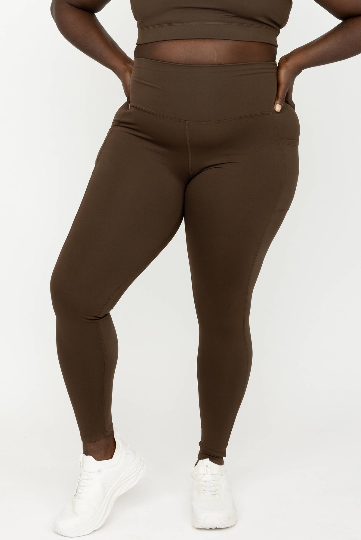 A model wearing high-waisted Chocolate Brown SuperHold Ankle Leggings, paired with white sneakers, shown from the waist down against a plain white studio background.