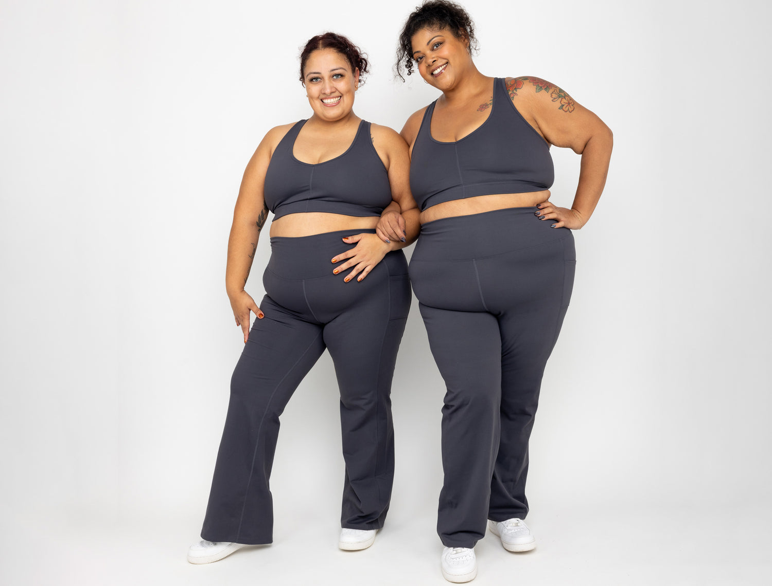 Two smiling models wearing matching Superfit Hero sets - bra and flare leggings in sizes 2X and 3X