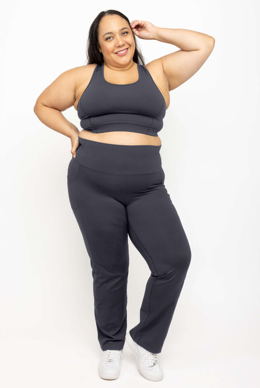 Smiling model wearing Superfit Hero SuperHold™ straight leggings and matching racerback sports bra in Carbon color, size 2X