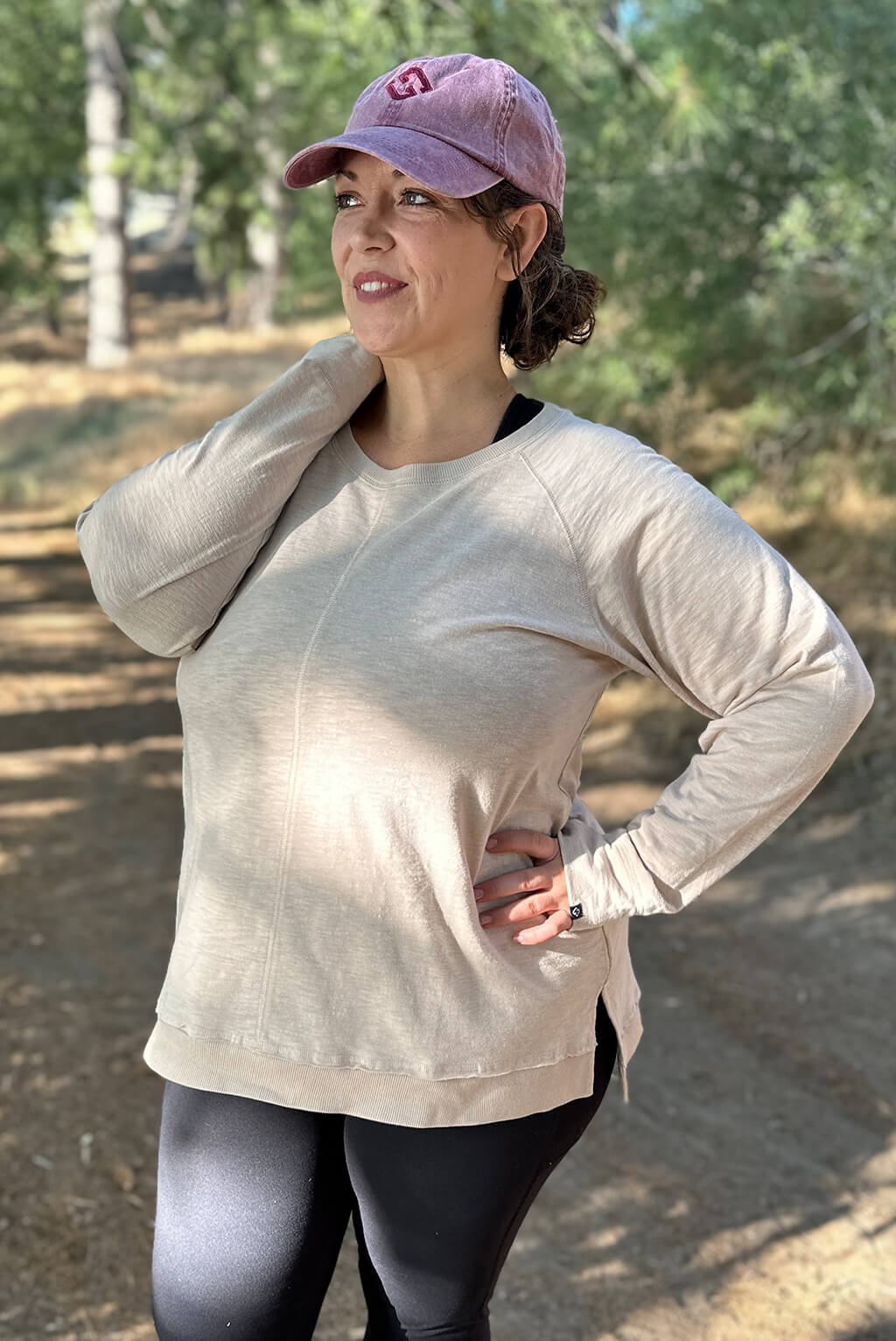 Plus size model poses on trail wearing long sleeve textured top and hat.