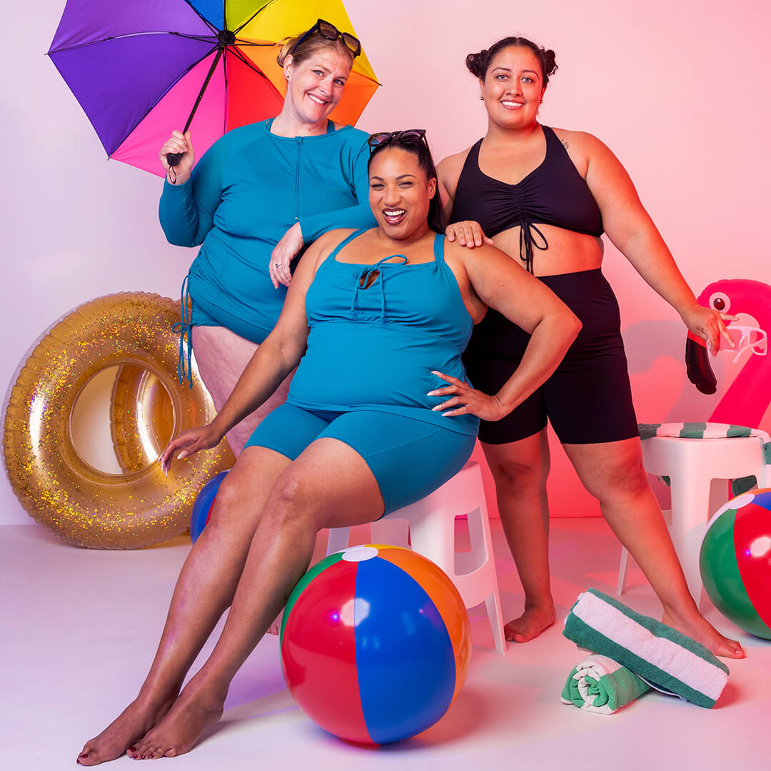 Three happy models wearing Superfit Hero swim separates with beachballs and floaties
