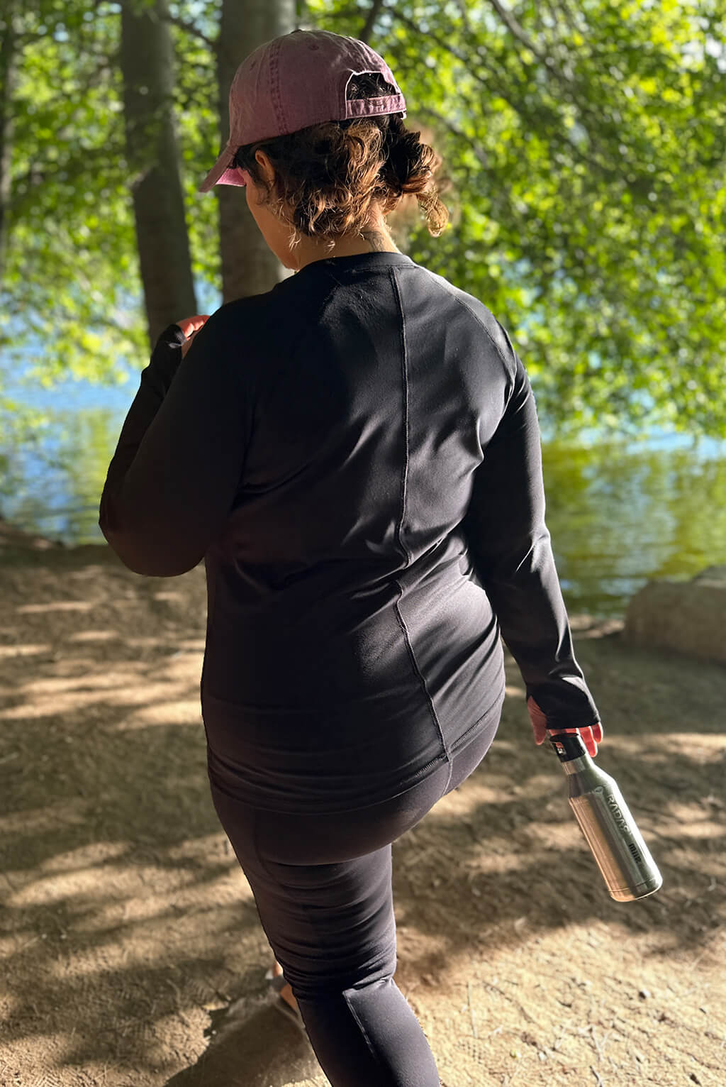 Back view of model walking in the woods wearing long sleeve compression top.