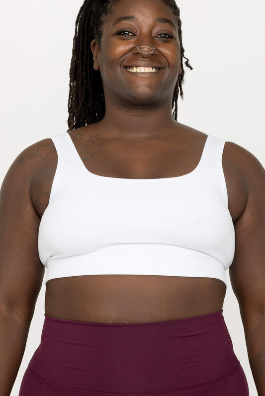 A smiling woman wearing a White SuperHold Scoop Bra and a high-waisted burgundy leggings, shown from the chest up against a plain light background.